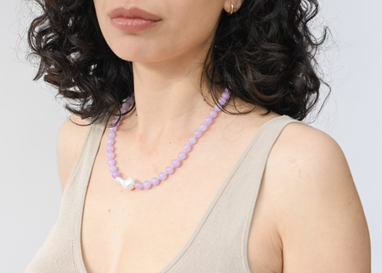 Woman wearing a beige tank top and a purple beaded necklace against a light gray background