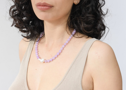 Woman wearing a beige tank top and a purple beaded necklace against a light gray background